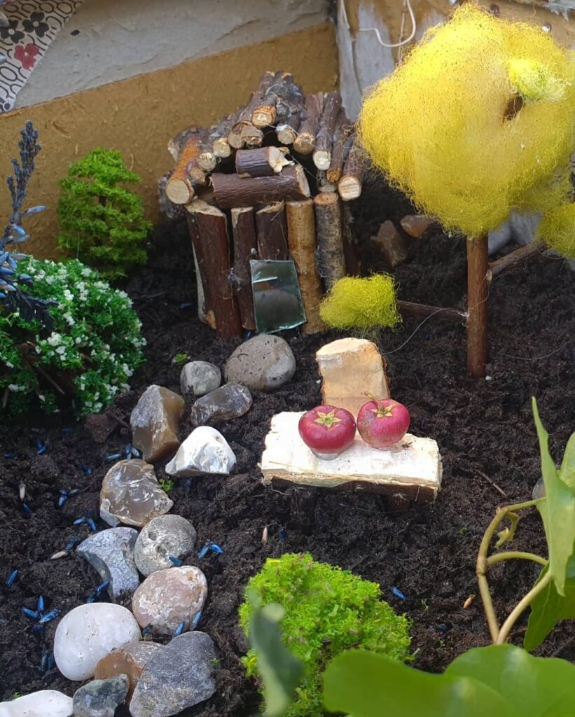 A whimsical miniature garden scene, with yellow cotton tree and a tiny wooden bench with two red fruits