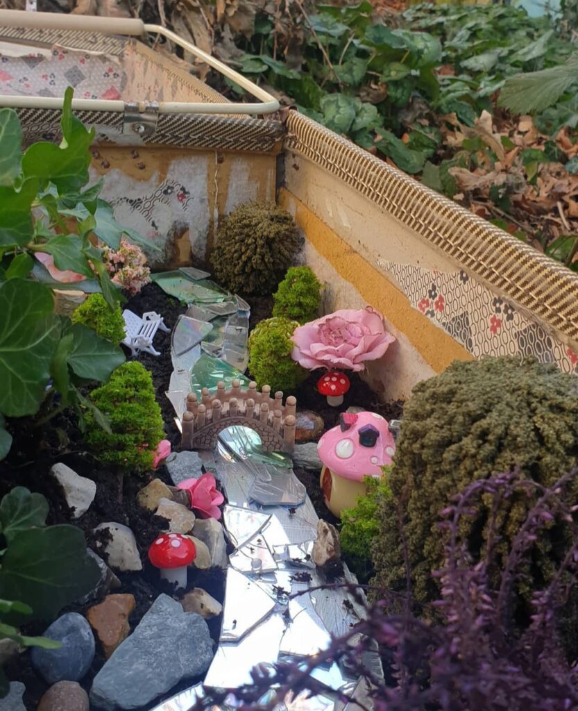 A whimsical miniature garden scene, made of fairy-tale elements like mushrooms, pink flowers, and moss.
